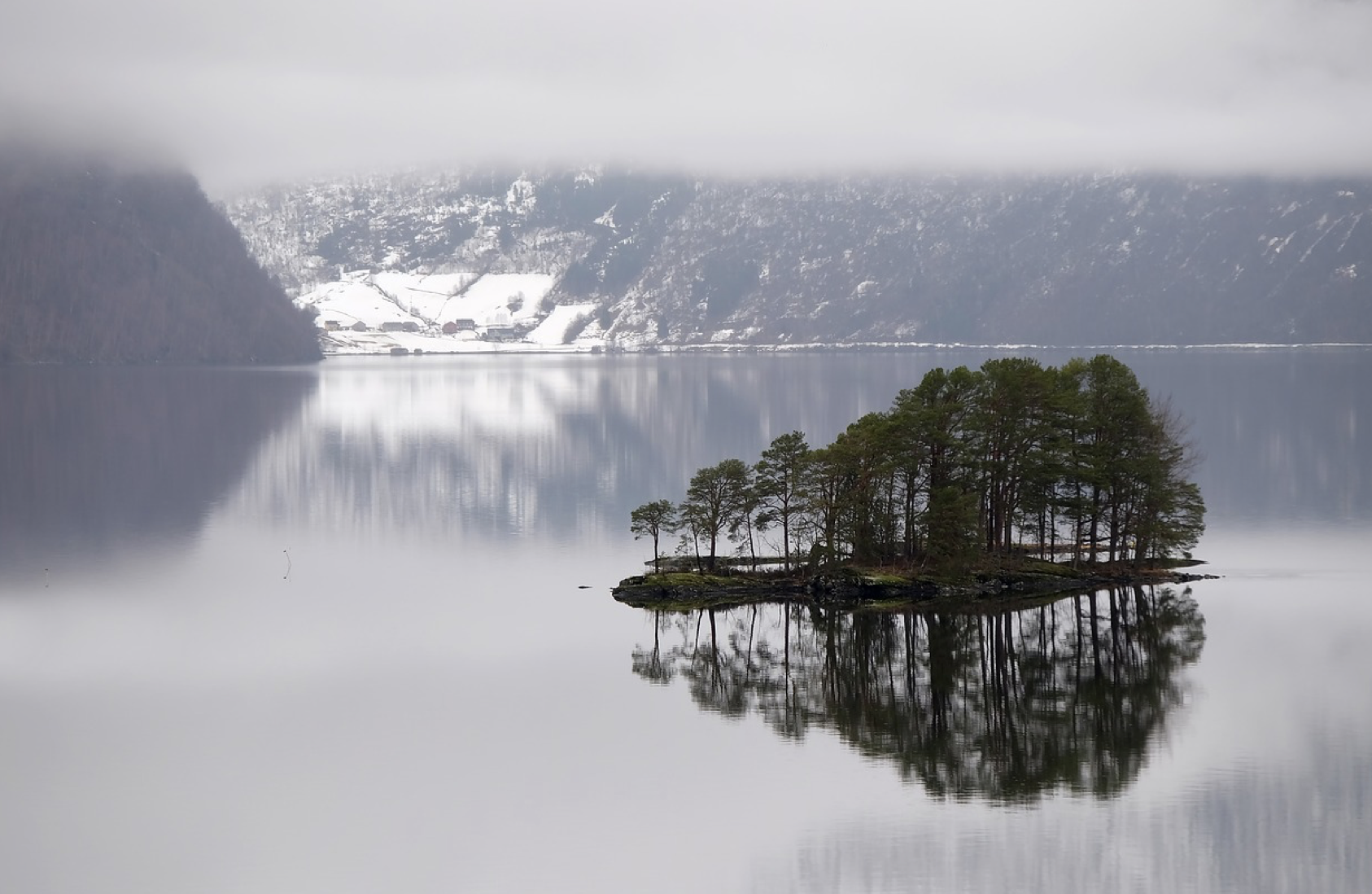 Image of a lake during the winter with a small island reflecting on the calm water.